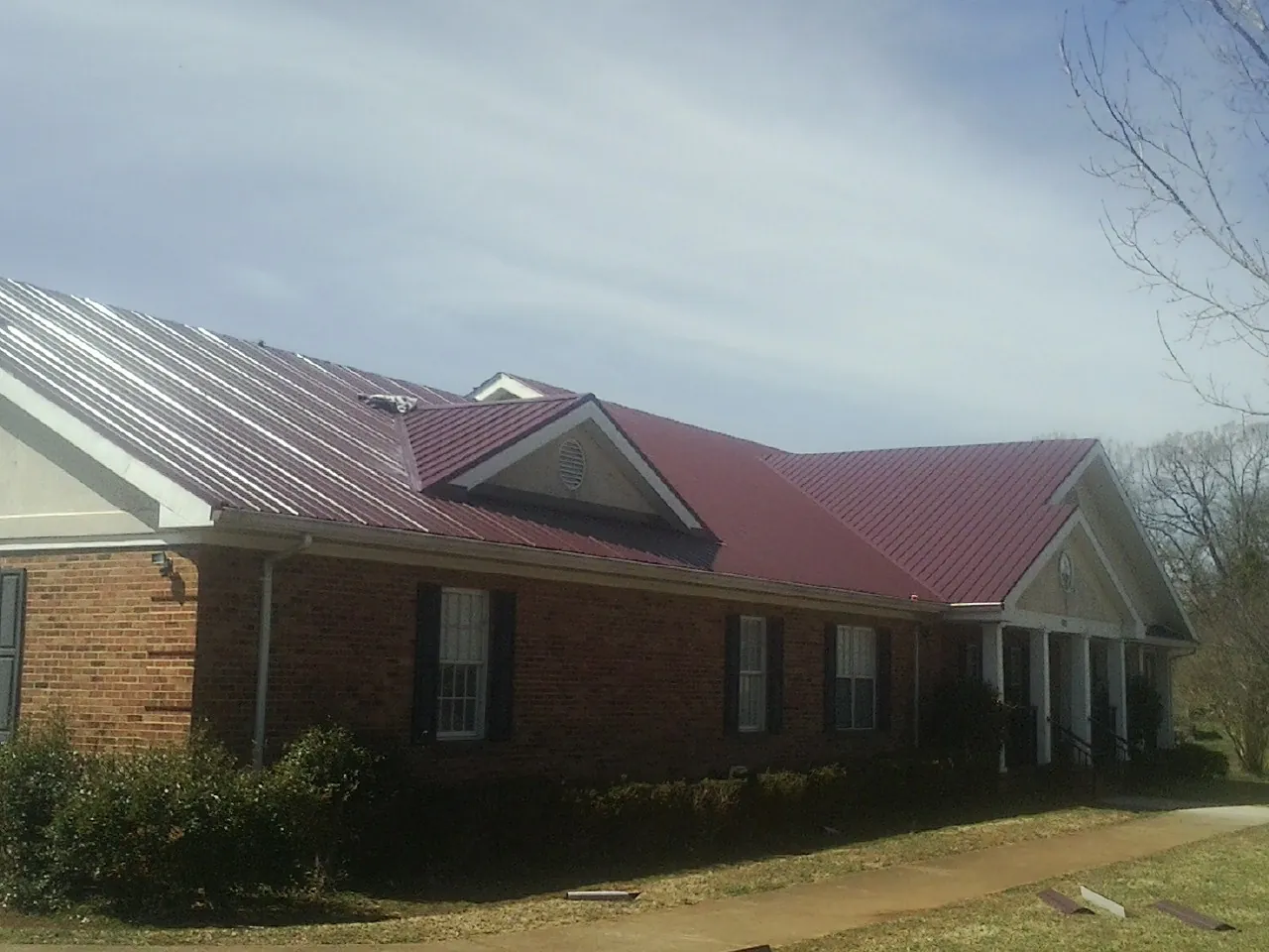 Red metal roof with gabled entries on a long brick building, from a Hail Damage Roof Repair job in Stevenson
